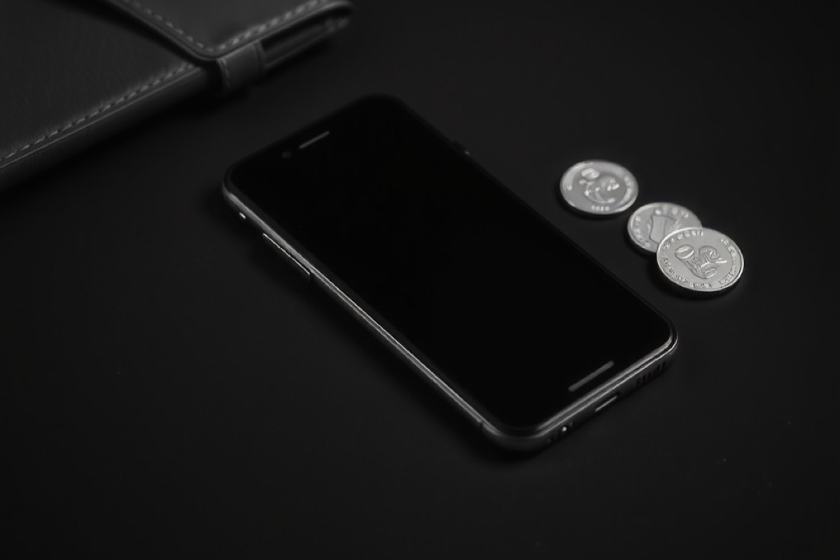 A smartphone on a dark desk beside a leather wallet and a few coins