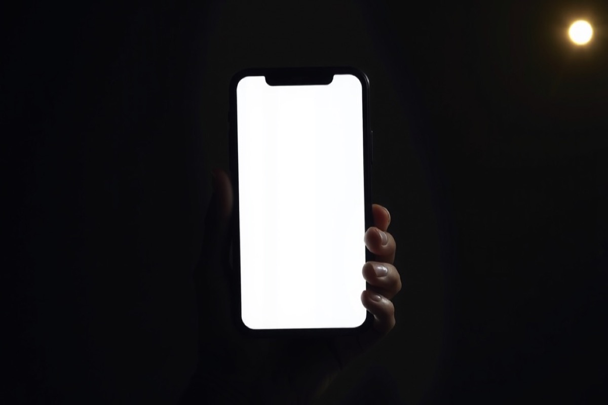 A hand holding a glowing smartphone against soft out-of-focus lights