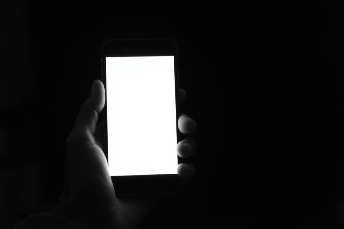 A hand holding a smartphone whose bright screen lights the fingers